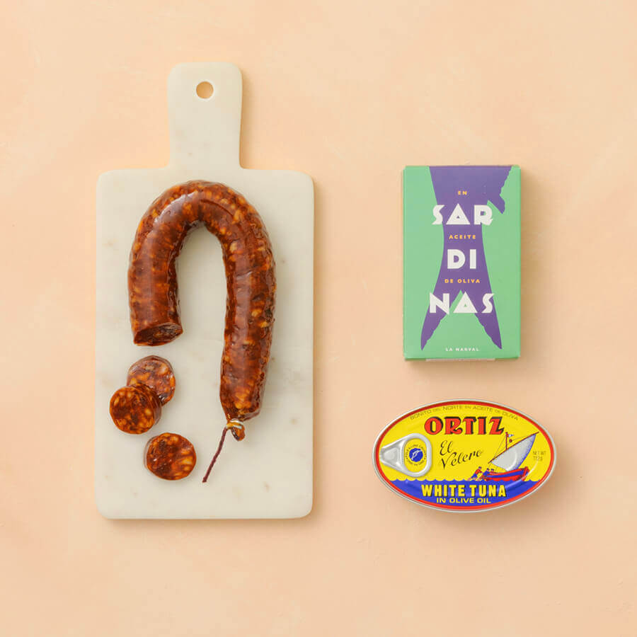 Chorizo on a marble cutting board with two tins of fish on a natural background