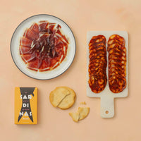 Plated cured Ibérico meat, sliced chorizo on a board, and crackers on a beige background
