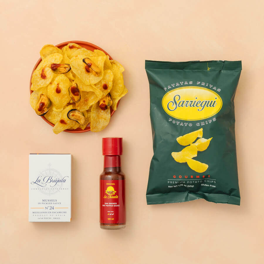 Sarriegui potato chips packaging with a bowl of chips, La Brujula sardines and La chinata hot sauce on a beige background.