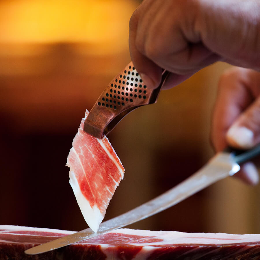 Person cutting a block of cured meat with a knife